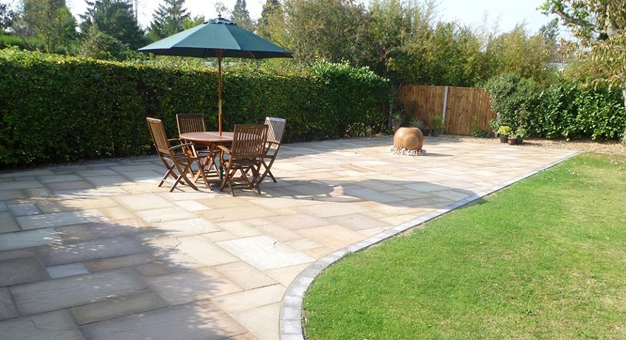 A patio laid by knights Paving and Landscaping with some wooden furniture and a parasol