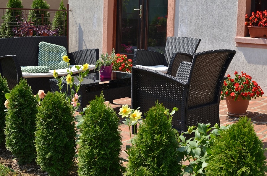 A garden patio with woven garden furniture, surrounded by small shrubs