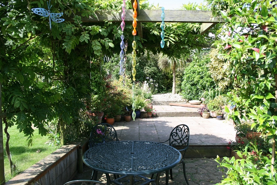 A Garden patio shaded by climbing plants, with pots and windchimes handing