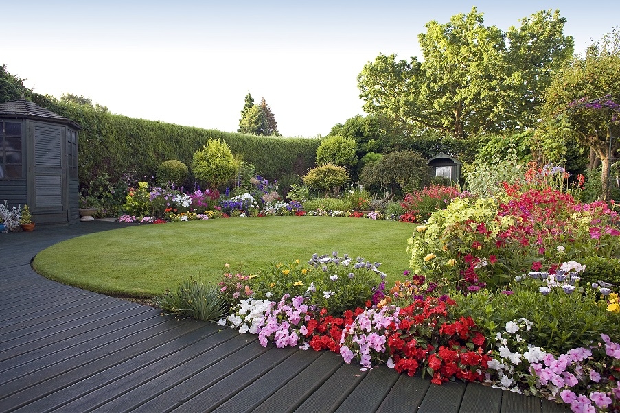 A garden with a decked pathway and small lawn, surrounded by a flower patch